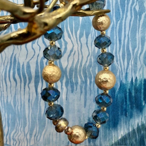 Bracelet élastique asymétrique composé de perles en cristal bleu et de perles en laiton martelé or. Bracelet bohème chic de créateur.